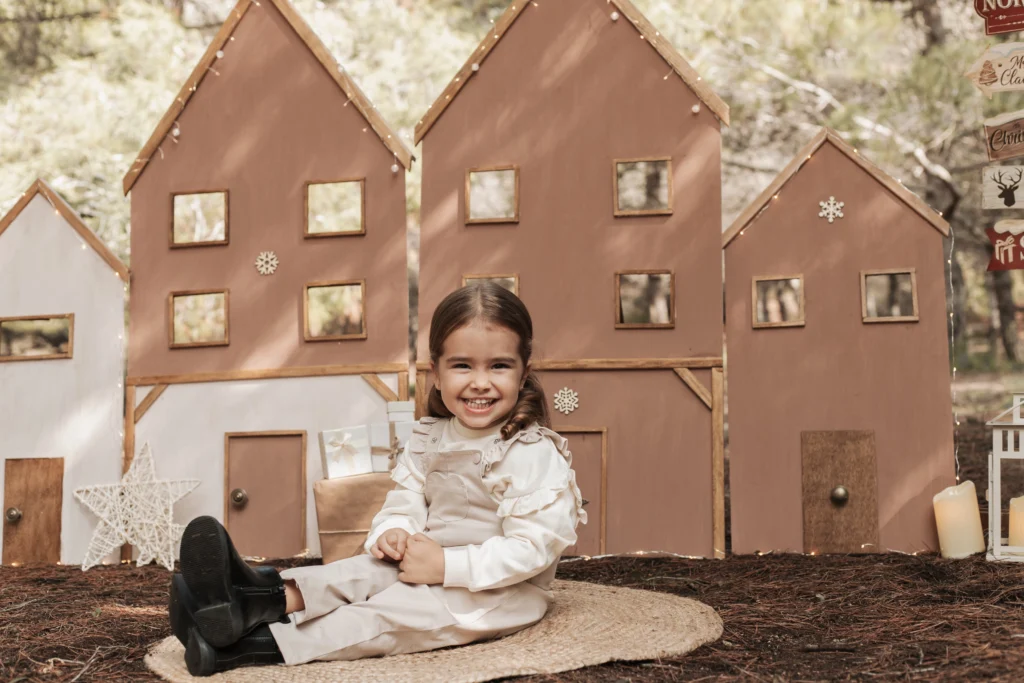 Sesión de Navidad infantil en exterior en Barcelona, niña sonriendo en decorado navideño de madera
