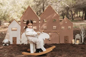 Niña en sesión de fotos de Navidad en exterior en Barcelona, jugando en un caballito de madera con decorado festivo